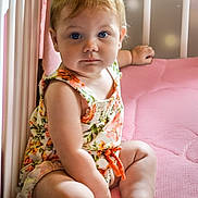 Sophia joined the competition — help win amazing prizes! baby, child, infant, blue_eyes, floral_romper, crib, pink_mattress, sitting, curious_expression, indoor, soft_lighting, cute, person, skin, legs, hand, headband, furniture, portrait, young