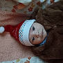 baby, brown_clothing, child, colorful, cute, eyes, face, festive, headwear, holiday, indoors, infant, lying_down, polka_dots, portrait, santa_hat, soft_texture, towel, winter_clothing, young_child