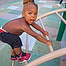 black_shorts, child, climbing, earring, expression, face, fence, hair_bun, metal_bars, outdoor, park, play_structure, playground, portrait, recreation, red_shoes, safety_surface, sneakers, surprised, toddler