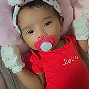 Ashley is registered to the contest to win money with this photo: baby, baby_clothing, bed, blanket, bow, cartoon, child, close_up, cute, face, headband, indoors, infant, lying_down, mittens, pacifier, pink_bedding, portrait, red_outfit, smiling