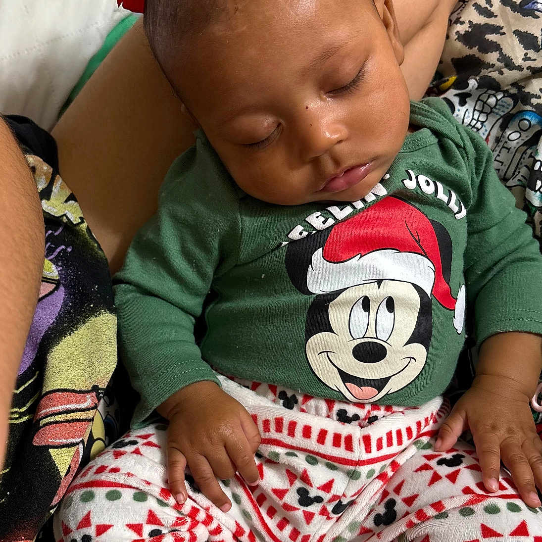 Keauni U is registered to the contest to win money with this photo: baby, blanket, child, closeup, comfort, cute, family, green_shirt, holiday_clothing, indoor, infant, mickey_mouse, pajamas, patterned_pants, peaceful, person, red_bows, resting, sleeping, socks