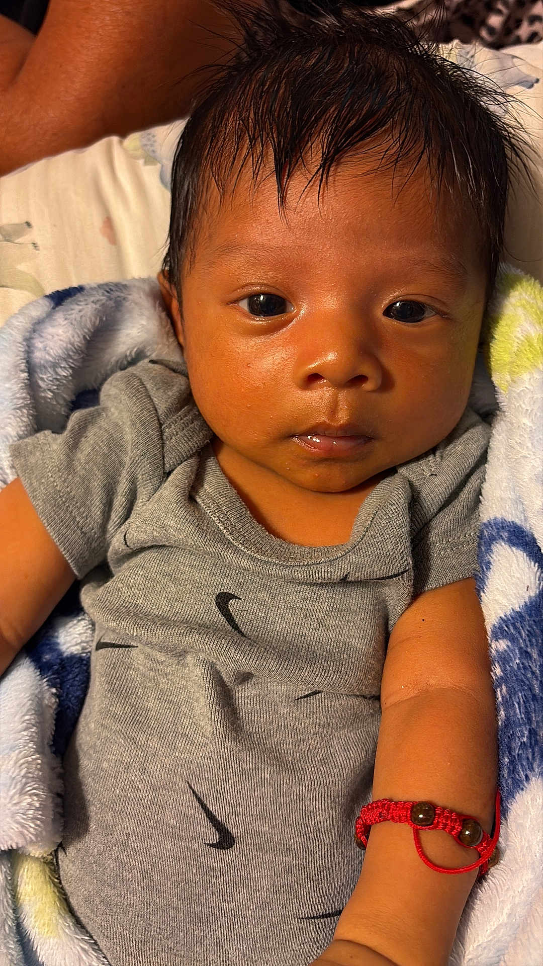 Juan joined the competition — help win amazing prizes! baby, infant, child, face, arm, bracelet, clothing, onesie, blanket, soft_texture, looking, portrait, skin, hair, close_up, laying, cute, indoor, person, young