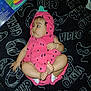 Ahtziri is registered to the contest to win money with this photo: baby, infant, pink_clothing, strawberry_costume, blanket, black_background, video_game_theme, doodles, text, cute, child, feet, hands, diaper, portrait, laying_down, looking_sideways, indoor, soft_toys, playful