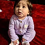 baby, child, infant, purple_clothing, knitwear, sitting, red_blanket, plush, cute, hands, feet, socks, portrait, indoors, expression, looking_up, face, hair, buttoned_sweater, earrings