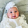 baby, infant, face, blue_eyes, headband, flower, white_clothing, lace, soft_blanket, gray_blanket, cute, chubby_cheeks, portrait, lying_down, closeup, child, adorable, person, young, smiling