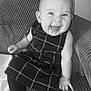 baby, smiling, child, dress, leggings, couch, happy, face, sitting, indoors, person, cute, infant, pattern, texture, monochrome, black_and_white, joy, small_hand, cozy