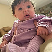 Kleo joined the competition — help win amazing prizes! baby, infant, child, purple_clothing, hand, face, indoor, person, curious, wide_eyes, holding, sitting, cozy, home, couch, fireplace, furniture, warm_lighting, human, portrait