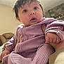 baby, infant, child, purple_clothing, hand, face, indoor, person, curious, wide_eyes, holding, sitting, cozy, home, couch, fireplace, furniture, warm_lighting, human, portrait