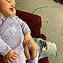 baby, sleeping, onesie, hand_holding, drool, cushion, carpet, indoor, child, casual_clothing, adult_hand, comfort, relaxation, resting, purple_clothing, butterfly_print, toy, distressed_jeans, floor, cozy