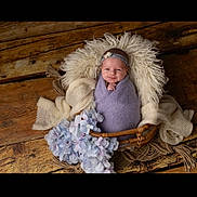 Mya a rejoint le concours — aidez-le/la à gagner de superbes lots ! baby, infant, wrapped, blanket, basket, headband, flower, wooden_floor, soft_texture, purple, white, smile, portrait, cozy, cute, newborn, decor, flooring, furniture, indoor