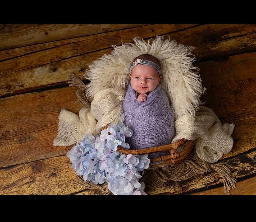 Mya a rejoint le concours — aidez-le/la à gagner de superbes lots ! baby, infant, wrapped, blanket, basket, headband, flower, wooden_floor, soft_texture, purple, white, smile, portrait, cozy, cute, newborn, decor, flooring, furniture, indoor
