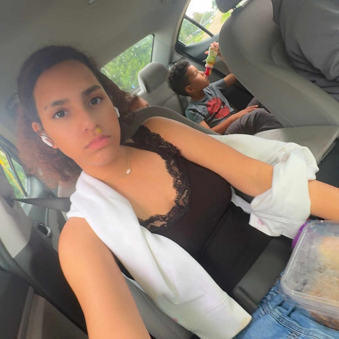 Lily is registered to the contest to win money with this photo: bottle, car, casual, child, children, clothing, drink, earbuds, family, hair, interior, jeans, person, portrait, road_trip, seat, seatbelt, selfie, window, young_person