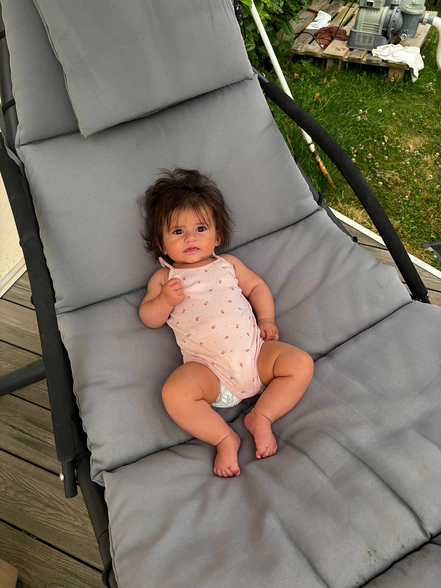 Lucia a rejoint le concours — aidez-le/la à gagner de superbes lots ! baby, child, infant, outdoor, lounge_chair, cushion, grass, wooden_deck, curious, pink_onesie, diaper, barefoot, wild_hair, person, relaxing, summer, garden, backyard, daylight, casual
