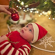 Maël a rejoint le concours — aidez-le/la à gagner de superbes lots ! baby, child, christmas, christmas_ornament, christmas_tree, cute, festive, floor, hand, holiday, holiday_decoration, indoors, looking_up, red_clothing, santa_hat, snowflake, striped_sleeves, tree_skirt, twinkling_lights, wooden_floor