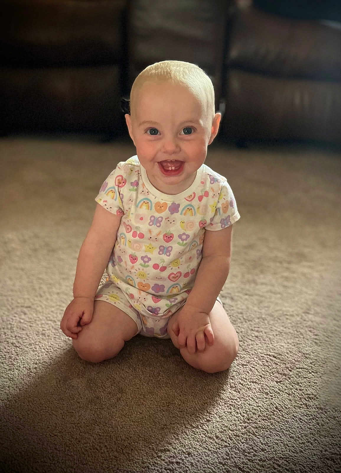 Raelynn is registered to the contest to win money with this photo: toddler, child, smile, happy, carpet, sitting, onesie, colorful_clothing, indoor, living_room, face, baby, cute, short_hair, bright_eyes, fun, playful, person, couch, background