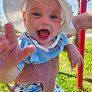 Raelynn is registered to the contest to win money with this photo: baby, child, smiling, hat, sunhat, blue_clothing, floral_pants, outdoor, green_grass, hand, person, happy, closeup, playground, sunlight, nature, cute, infant, reaching_hand, daytime