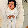 baby, infant, smiling, curly_hair, white_onesie, cushion, soft_texture, indoor, happy, child, cute, portrait, lying_down, cozy, comfort, bright_eyes, infant_clothing, baby_bed, small_hands, joyful