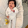baby, infant, smiling, curly_hair, onesie, balloon, confetti, cushion, plush, indoor, happy, child, person, waving, cozy, footed_pajamas, cute, portrait, soft_texture, celebration