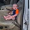 baby, child, vehicle, car, leather_seat, open_door, orange_clothing, blue_clothing, infant, sitting, interior, suburban, house, window, seatbelt, door_frame, sidewalk, curious, person, casual