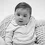 baby, infant, child, face, portrait, black_and_white, clothing, sweatshirt, pants, cushion, knitted, texture, seated, indoors, cute, young, expression, looking, soft_lighting, closeup