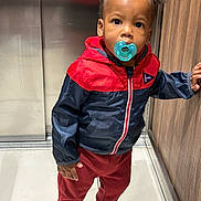 Djanhaël a rejoint le concours — aidez-le/la à gagner de superbes lots ! toddler, child, pacifier, jacket, red_pants, sneakers, standing, elevator, floor_tiles, hand_on_wall, curly_hair, indoor, casual_clothing, young_child, portrait, real_photo, looking_at_camera, expression, small_child, person
