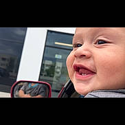 Alejandro is registered to the contest to win money with this photo: baby, infant, child, smiling, gummy_smile, face, portrait, close_up, car, vehicle, side_mirror, outdoor, daylight, building, window, reflection, gray_clothing, happy, candid, photography
