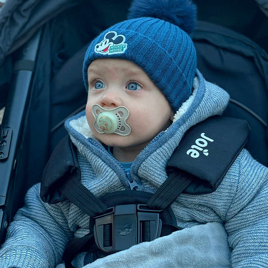Ollee is registered to the contest to win money with this photo: baby, baby_boy, blanket, blue_hat, child, curious, cute, face, hands, infant, jacket, mickey_mouse, outdoor, pacifier, portrait, seated, straps, stroller, warm_clothing, winter