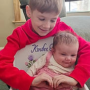 Kinslee joined the competition — help win amazing prizes! child, baby, sibling, indoor, smile, red_hoodie, pink_dress, white_tights, chair, window, green_armchair, happy, family, baby_rocker, holding, cute, portrait, infant, toddler, home