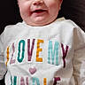 baby, smiling, child, sweatshirt, colorful_text, denim_pants, casual_clothing, portrait, cute, happy, infant, lying_down, indoors, comfortable, joyful, person, face, young_child, apparel, love_message