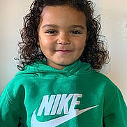 Aaveleiio is registered to the contest to win money with this photo: child, curly_hair, green_hoodie, nike_logo, smiling, portrait, casual_clothing, indoor, person, young_child, face, happy, head_and_shoulders, fashion, cute, childhood, expression, clothing, studio_light, background