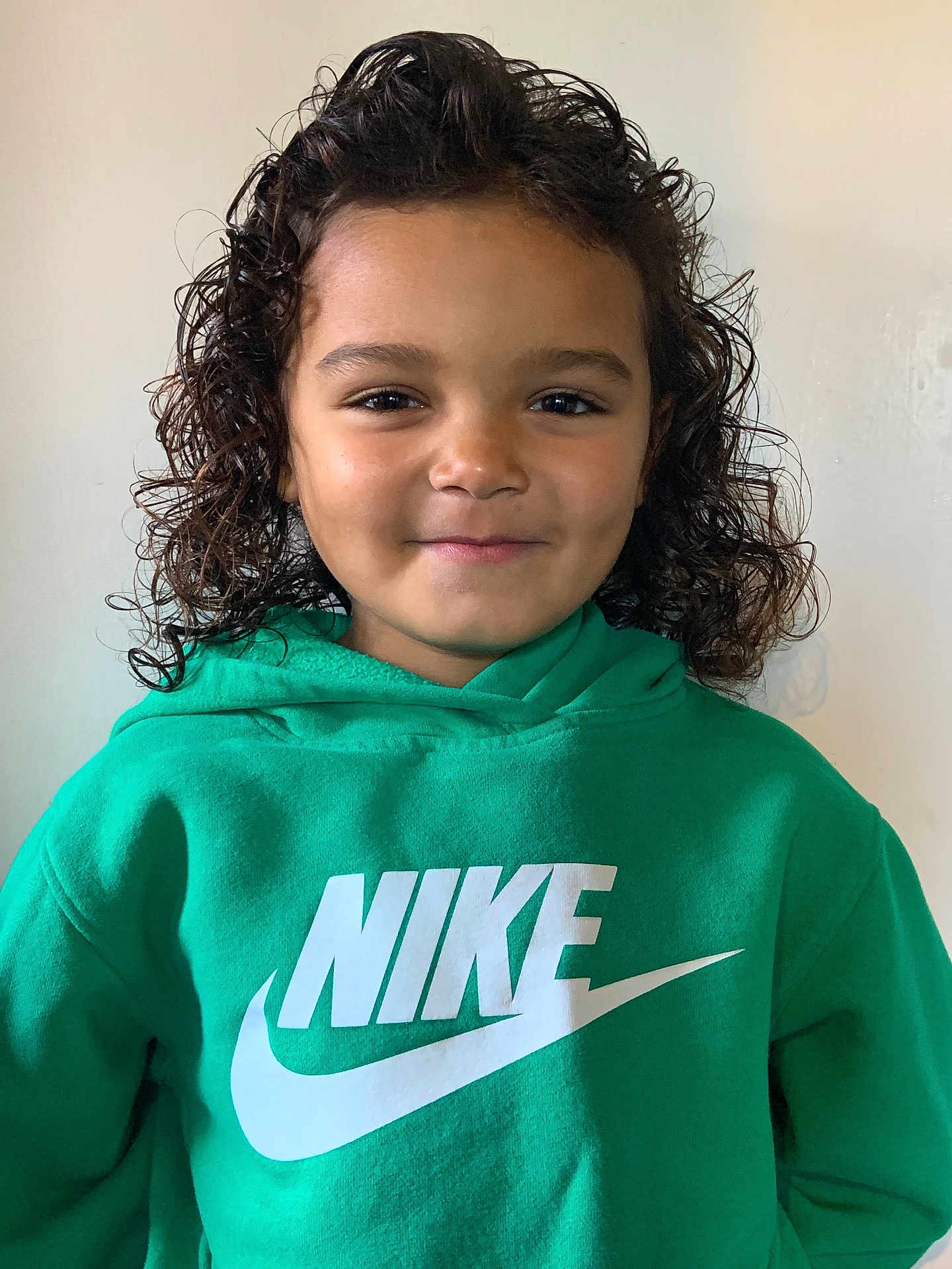 Aaveleiio is registered to the contest to win money with this photo: child, curly_hair, green_hoodie, nike_logo, smiling, portrait, casual_clothing, indoor, person, young_child, face, happy, head_and_shoulders, fashion, cute, childhood, expression, clothing, studio_light, background