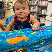 River joined the competition — help win amazing prizes! baby, child, smiling, shopping_cart, store, aisle, colorful, clothing, face, person, sitting, blue, pattern, toy, playful, cheeky, happy, retail, infant, cover