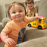 Weston joined the competition — help win amazing prizes! toddler, child, indoor, toy, bus, couch, playing, smiling, person, short_hair, orange_shirt, brown_shirt, furniture, carpet, window_blinds, happy, cute, baby, home, floor