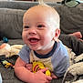baby, blanket, blue_shirt, child, close_up, clothing, couch, expression, face, happy, holding, home, indoor, infant, person, playful, skin, smiling, soft_toys, toys