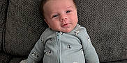 Ryder joined the competition — help win amazing prizes! baby, infant, newborn, couch, onesie, mittens, face, head, smile, sitting, upholstery, texture, pattern, zipper, clothing, indoor, portrait, cozy, adorable, relaxed