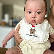 Oliver is registered to the contest to win money with this photo: baby, infant, child, bib, clothing, person, cute, face, indoors, holding, human, skin, expression, chubby, young, smile, apparel, head, eyes, funny_text