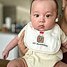 baby, infant, child, bib, clothing, person, cute, face, indoors, holding, human, skin, expression, chubby, young, smile, apparel, head, eyes, funny_text