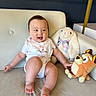 baby, bib, bunny, child, clothing, couch, cute, decor, dog_toy, furniture, happy, home, indoor, infant, person, plush_toy, sitting, smiling, stuffed_animal, toy