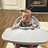 Oliver is registered to the contest to win money with this photo: baby, high_chair, infant, face, hands, tray, curious, indoor, wooden_floor, fireplace, bib, clothing, person, foot, carpet, home, expression, sitting, child, young