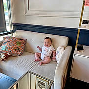 Oliver is registered to the contest to win money with this photo: baby, baby_sitting, bib, cabinet, child, clothing, couch, face, floor, furniture, home_decor, indoor, pillow, reflection, smiling, stuffed_animal, table, toy, wall, window