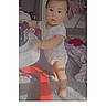 baby, child, toddler, standing, portrait, face, smiling, indoors, playroom, toy, furniture, carpet, clothing, onesie, barefoot, nursery, house, heart_sticker, text_overlay, photograph