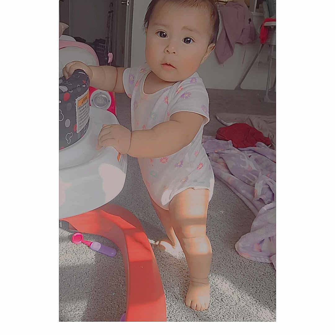 Ashley Isaguirre is registered to the contest to win money with this photo: baby, child, toddler, standing, portrait, face, smiling, indoors, playroom, toy, furniture, carpet, clothing, onesie, barefoot, nursery, house, heart_sticker, text_overlay, photograph