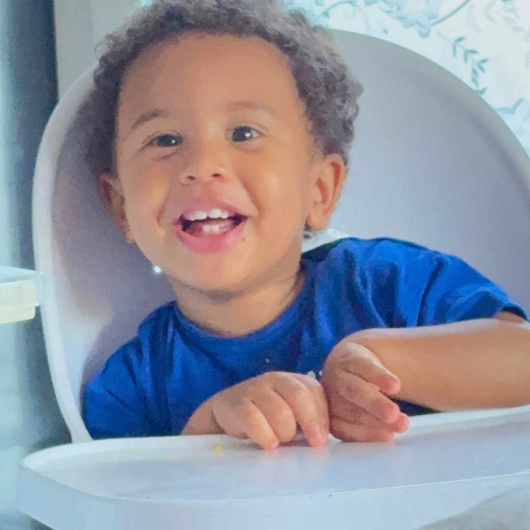 Kalil Keita participe au concours pour gagner de l'argent avec cette photo : baby, blue_shirt, child, curly_hair, cute, daylight, face, hands, happy, high_chair, home, indoor, person, portrait, seated, smiling, table, toddler, window, young_child