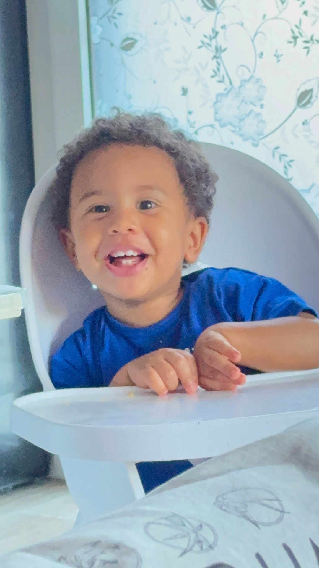 Kalil Keita participe au concours pour gagner de l'argent avec cette photo : baby, blue_shirt, child, curly_hair, cute, daylight, face, hands, happy, high_chair, home, indoor, person, portrait, seated, smiling, table, toddler, window, young_child