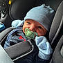 baby, car_seat, pacifier, blue_hat, mittens, infant, child, seatbelt, clothing, cute, face, eyes, closeup, indoor, soft_lighting, warm, smile, babywear, newborn, comfort