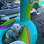 dog, white_dog, inflatable, parrot_float, pool, lounge_chair, swimming_pool, pet, collar, summer, vacation, outdoor, concrete, towel, sunbathing, people, greenery, relaxation, toy, shade