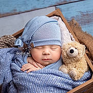 Owen is registered to the contest to win money with this photo: newborn, baby, sleeping, blue_hat, blue_blanket, wooden_crate, teddy_bear, soft_texture, cozy, infant, cute, portrait, peaceful, wrapped, knit, child, resting, indoors, closeup, adorable