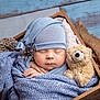 newborn, baby, sleeping, blue_hat, blue_blanket, wooden_crate, teddy_bear, soft_texture, cozy, infant, cute, portrait, peaceful, wrapped, knit, child, resting, indoors, closeup, adorable