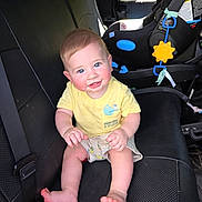 Camden is registered to the contest to win money with this photo: baby, black_leather, blue_eyes, car_interior, car_seat, child, cute, happy, indoors, infant, person, portrait, rosy_cheeks, seat_belt, shorts, sitting, smiling, sunlight, toy, yellow_shirt