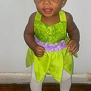 Jazlynn is registered to the contest to win money with this photo: baby, child, toddler, girl, green_dress, headband, purple_flowers, white_tights, pink_socks, standing, smiling, indoors, wooden_floor, plain_wall, cute, playful, earrings, portrait, happy, person